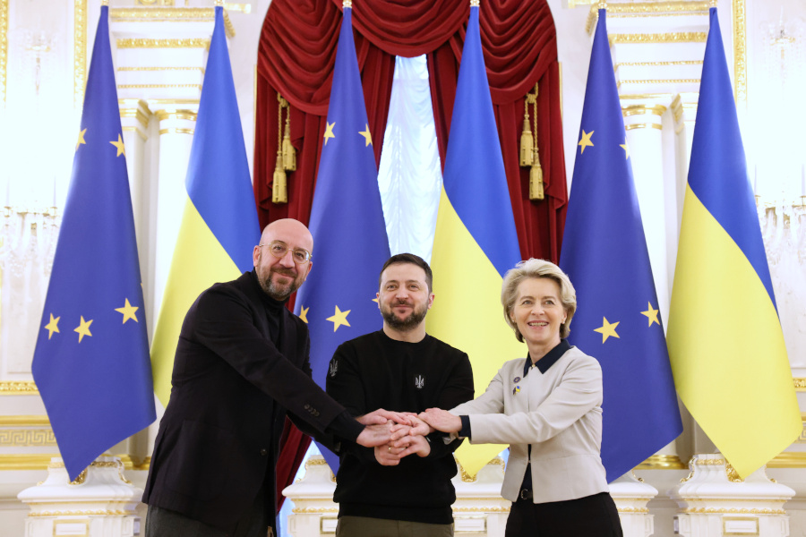 Der ukrainische Präsident steht mit Charles Michel, Präsident des Europäischen Rates, sowie Ursula von der Leyen, Präsidentin der Europäischen Kommission, mit überschlagenden Händen vor ukrainischen und EU-Flaggen