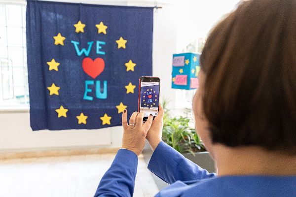 Eine Frau macht mit einem Smartphone ein Foto von einer Europa-Flagge