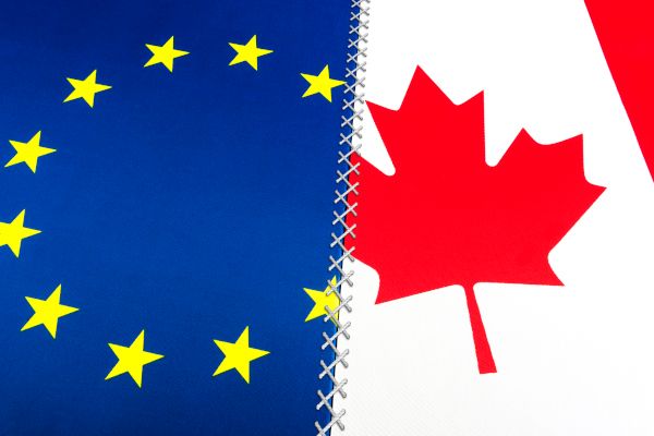 Abbildung Europa-Flagge (links in Bildhälfte) und Kanada-Flagge (rechts in Bildhälfte) - die Flaggen sind durch eine Naht in der Mitte "zusammengenäht"