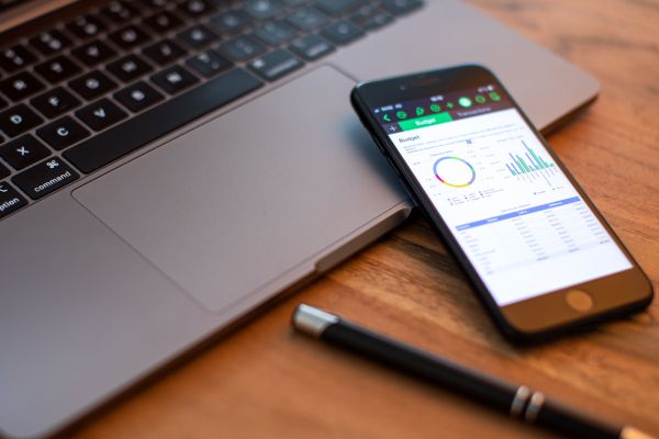 Ein Smartphone liegt auf einem Laptop, ein schwarzer Kugelschreiber liegt vor dem Laptop