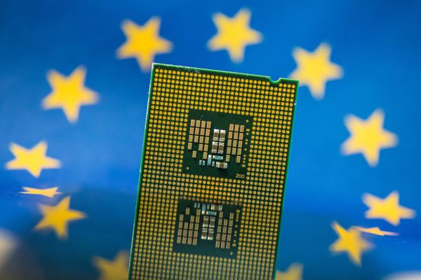 Am Bild zu sehen ist ein Halbleiterchip, im Hintergrund ist die EU-Flagge