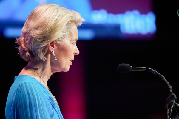 Ursula von der Leyen, Präsidentin der Europäischen Kommission, steht vor einem Mikrofon - sie trägt eine blaue Bluse