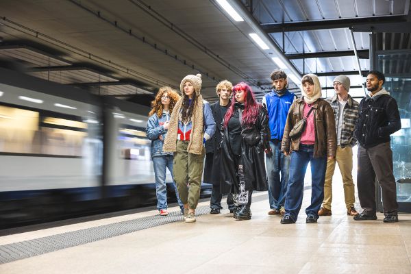 Jugendliche stehen am Bahnhof und sehen vorbeifahrendem Zug entgegen