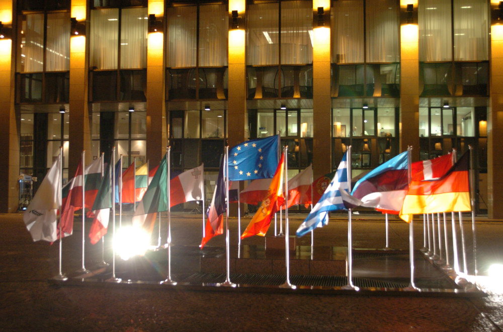 Verschiedene Flaggen auf einem kleinen Fahnenmast, vor einem Gebäude