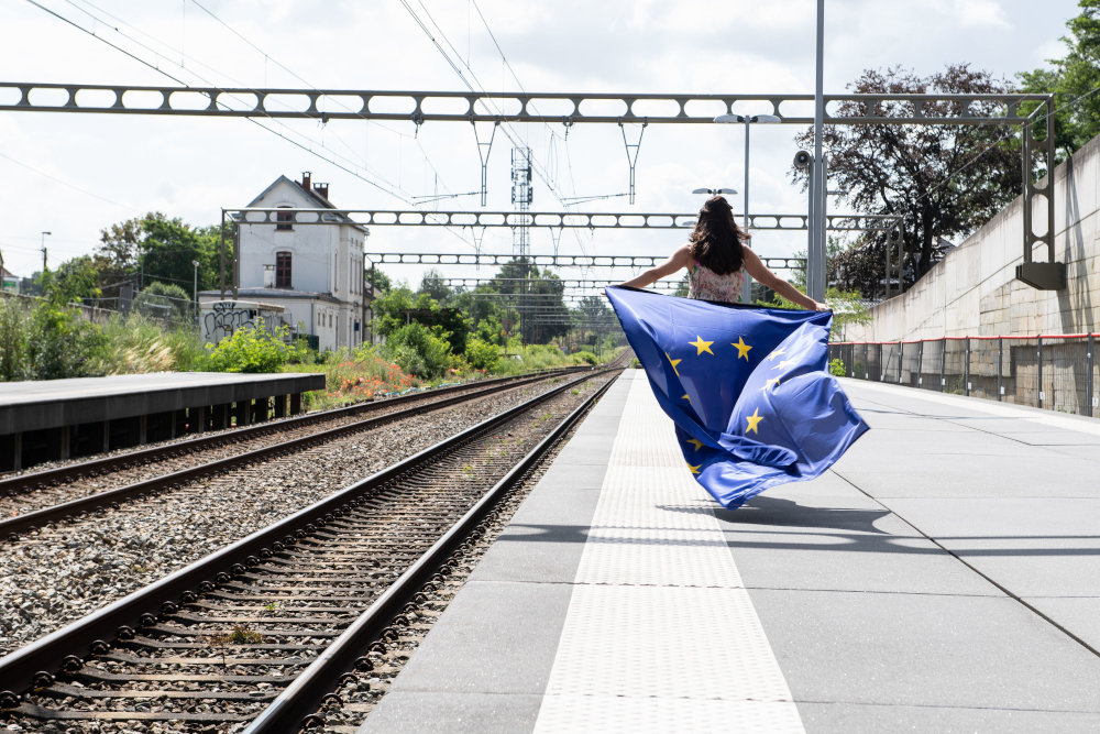 Eine Frau mit einer Flagge der Europäischen Union auf einem Bahnsteig