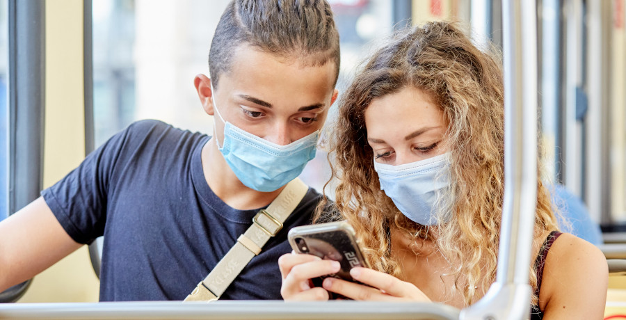 Teenagers couple with masks inside Milano tram watching smartphone