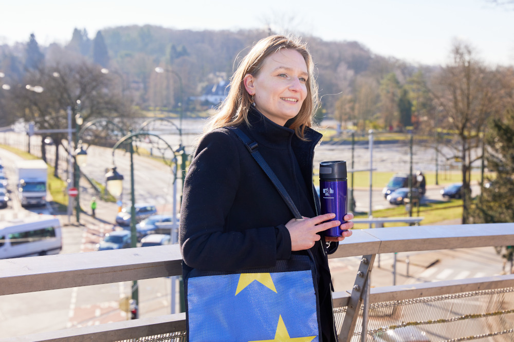 Eine Frau hält einen EU-Kaffeebecher und steht auf einer Brücke
